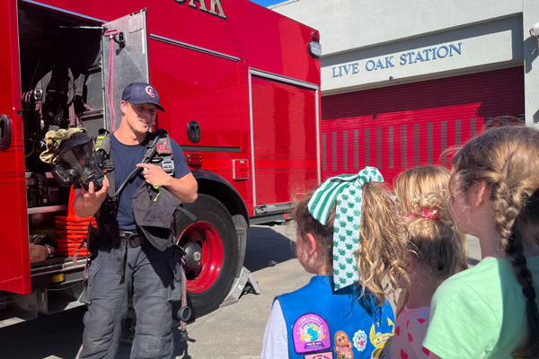 A firefighter showing the tools on a fire engine to a group of Girls Scouts.